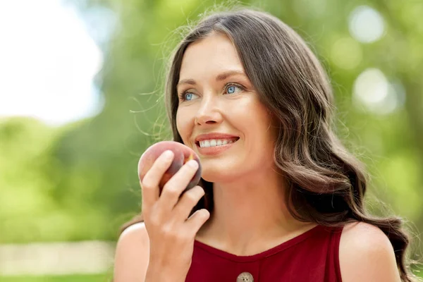 Glückliche Frau isst Pfirsich im Sommerpark — Stockfoto