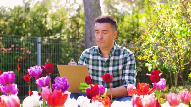 Man med Urklipp och blommor på sommaren trädgård — Stockvideo