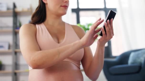 Happy pregnant woman with phone doing yoga at home — Stock Video