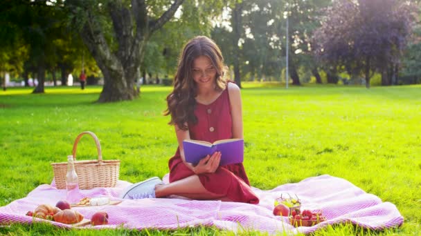 Lycklig kvinna läser bok på picknick i sommarparken — Stockvideo