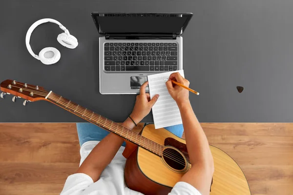 Man with guitar writing to music book at table — Stock Photo, Image