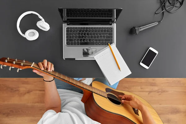 Young man with laptop playing guitar at table — Stock Photo, Image