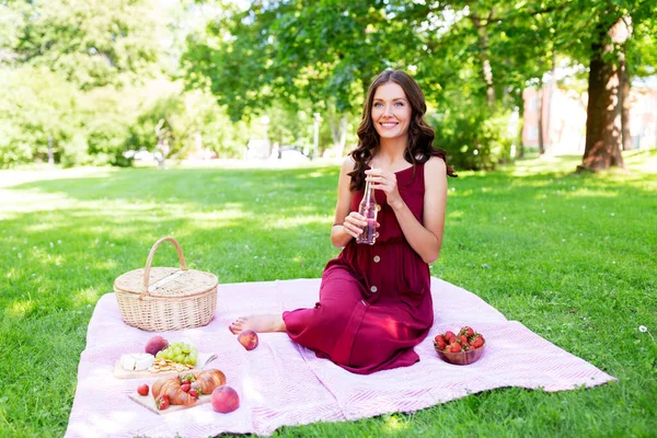 Gelukkig vrouw met picknick mand en drinken in park — Stockfoto