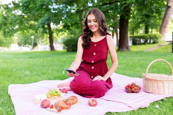 Mujer feliz con teléfono inteligente en el picnic en el parque — Foto de Stock