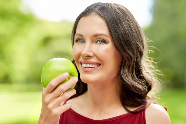 Lycklig kvinna äter grönt äpple i sommarparken — Stockfoto