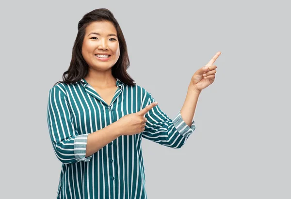 Glad asiatisk kvinna pekar finger upp på grå — Stockfoto