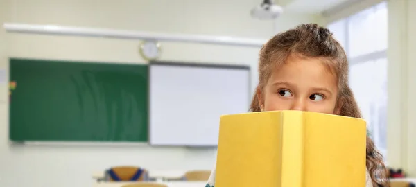 Petite fille cachée derrière livre jaune à l'école — Photo