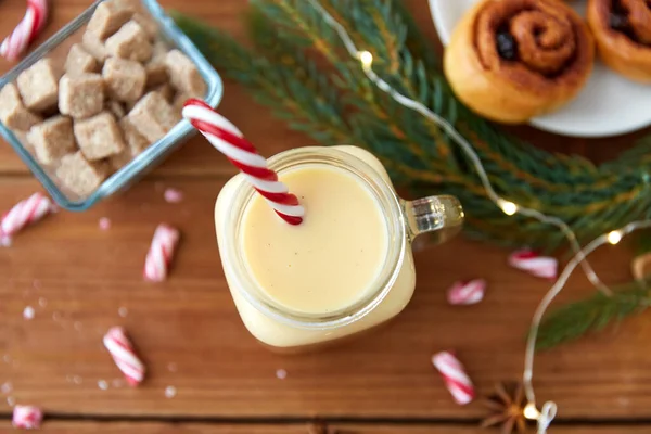 Ponche de huevo con bastón de caramelo en taza y bollos de canela — Foto de Stock