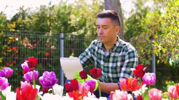 Mann mit Notizbuch und Blumen im Sommergarten — Stockvideo