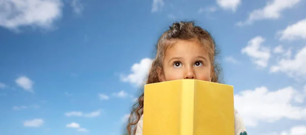 Little girl hiding behind book over sky and clouds — Stock Photo, Image