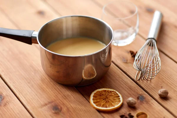 Pentola con zabaione, frusta e spezie su legno — Foto Stock