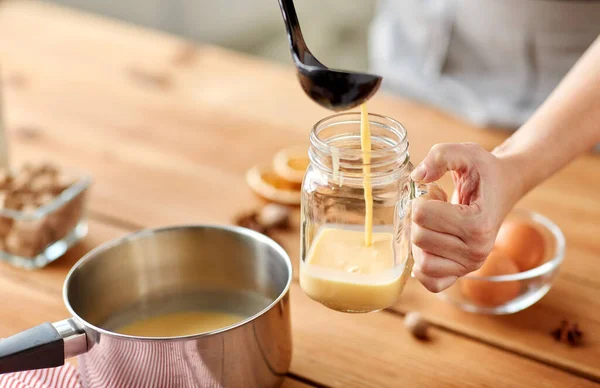 Händer med slev hälla äggtoddy från kastrull till glas — Stockfoto