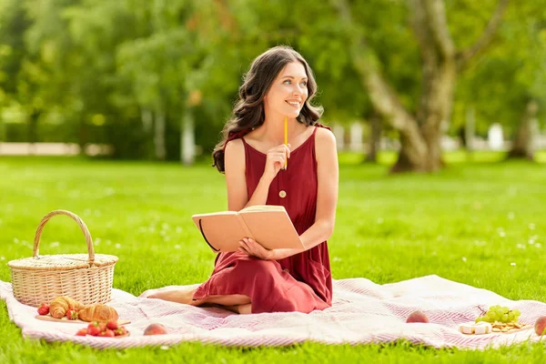 Szczęśliwa kobieta z pamiętnikiem i koszykiem piknikowym w parku — Zdjęcie stockowe
