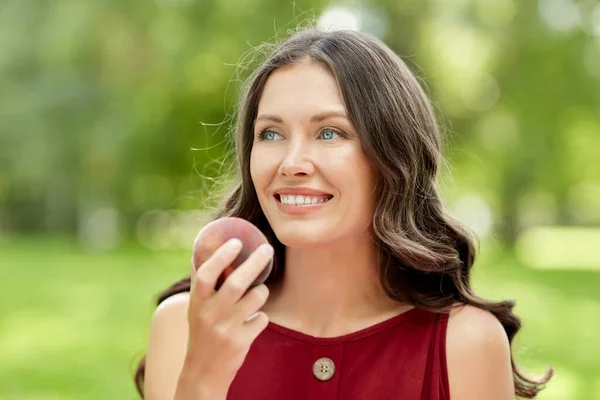 Happy woman eating peach at summer park — Stock Photo, Image