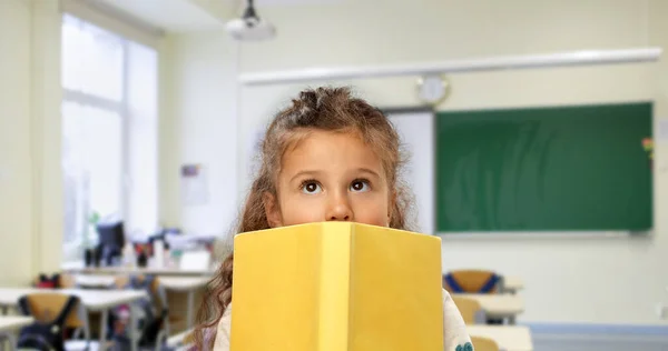 Menina se escondendo atrás do livro amarelo na escola — Fotografia de Stock