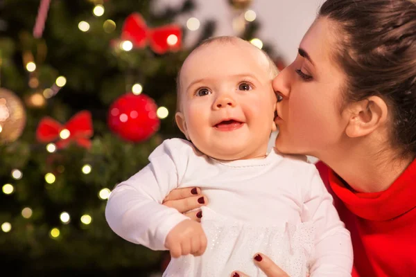크리스마스 트리 위에서 엄마가 아기 딸에게 키스하는 모습 — 스톡 사진