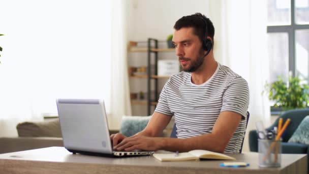 Mężczyzna z słuchawkami i laptopem pracujący w domu — Wideo stockowe