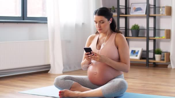 Zwanger vrouw met oortjes doet yoga thuis — Stockvideo