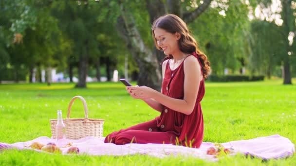 Šťastná žena s chytrým telefonem na piknik v parku — Stock video