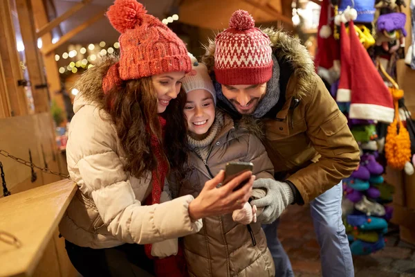 Lycklig familj med smartphone på julmarknaden — Stockfoto