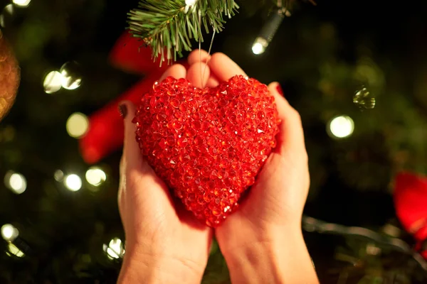 Mãos decorando árvore de natal com coração vermelho — Fotografia de Stock