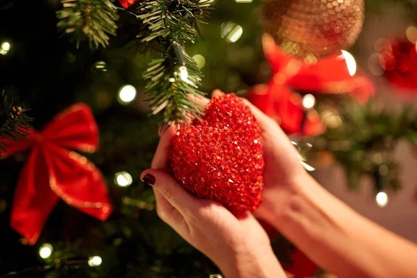 Hands decorating christmas tree with red heart — Stock Photo, Image