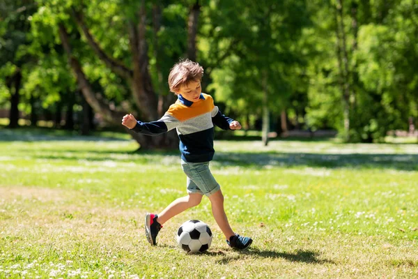 Счастливый мальчик с мячом играет в футбол в парке — стоковое фото