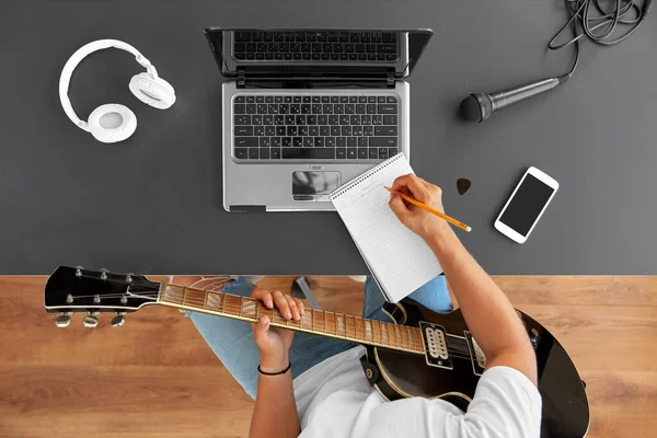 Man with guitar writing to music book at table — Stock Photo, Image