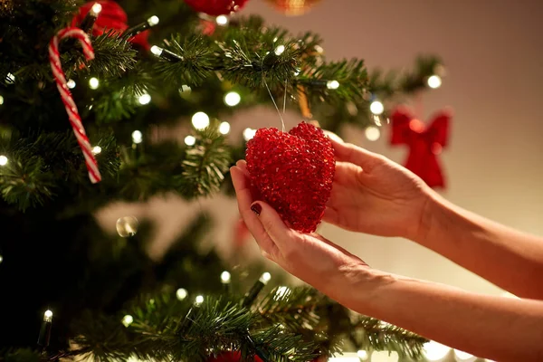 Mani che decorano l'albero di Natale con cuore rosso — Foto Stock