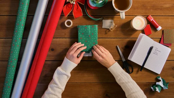 Руки заворачивая рождественский подарок в бумагу дома — стоковое фото