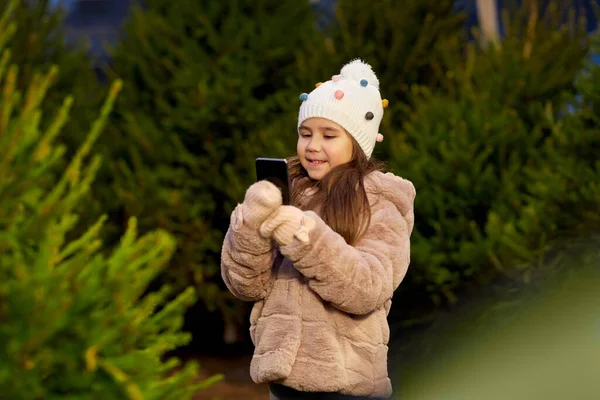 Dziewczyna ze smartfonem na rynku choinki — Zdjęcie stockowe