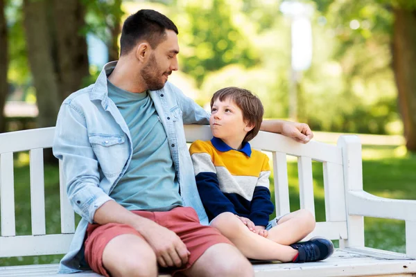 Padre con hijo sentado en el banco del parque y hablando —  Fotos de Stock