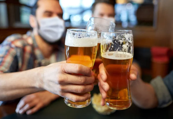 Amigos do sexo masculino em máscaras beber cerveja no bar ou pub — Fotografia de Stock