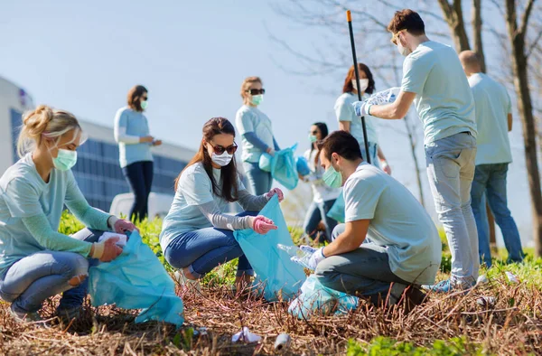 Vrijwilligers in maskers met zakken schoonmaken buiten — Stockfoto