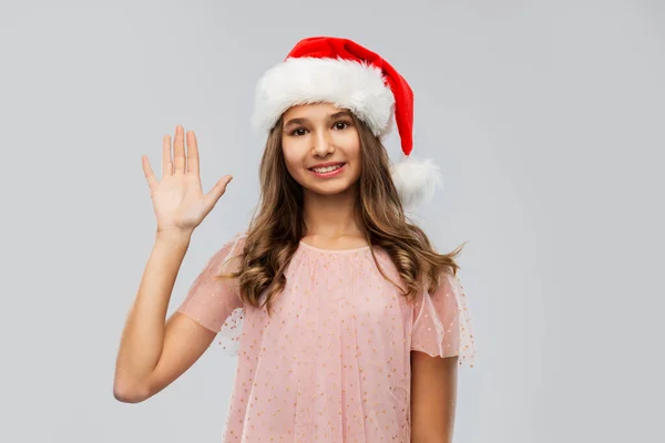 Happy teenage girl in santa hat waving hand — Stock Photo, Image