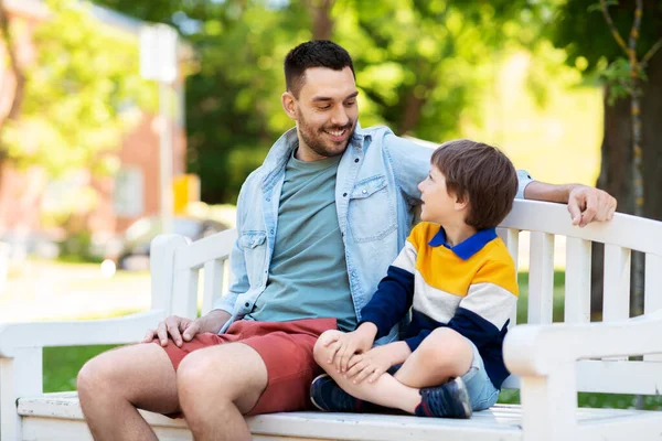 Padre con figlio seduto sulla panchina del parco e parlando — Foto Stock