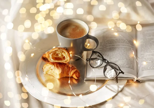 Croissanter, kaffe, bok och glas i sängen — Stockfoto