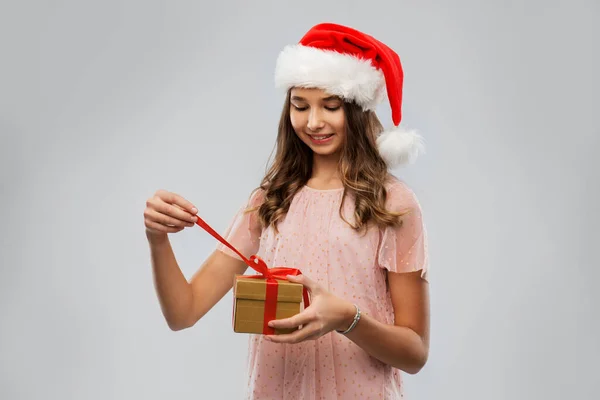 Teenage girl in santa hat opening christmas gift — Stock Photo, Image
