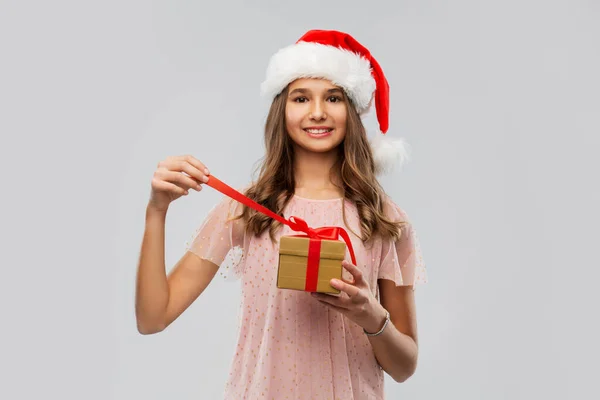 Adolescente em santa chapéu abrindo presente de Natal — Fotografia de Stock