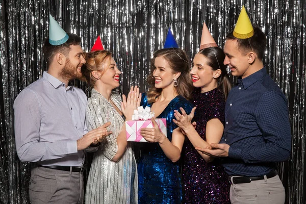 Amigos felices en sombreros de fiesta con regalo de cumpleaños —  Fotos de Stock