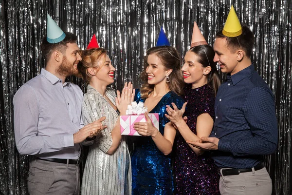 Amigos felizes em chapéus de festa com presente de aniversário — Fotografia de Stock