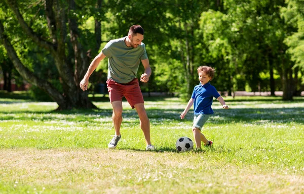 Отец с маленьким сыном играет в футбол в парке — стоковое фото