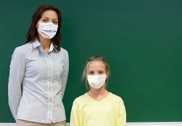 Estudiante chica y profesor en máscaras en la escuela —  Fotos de Stock