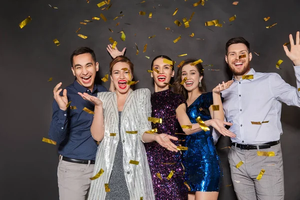 Amigos felices en la fiesta bajo confeti sobre negro — Foto de Stock