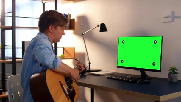 Ung man med dator spelar gitarr hemma — Stockvideo