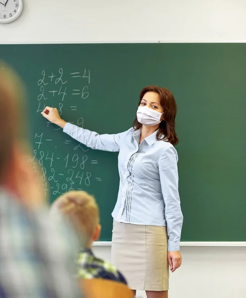 Учитель в маске писать на доске в школе — стоковое фото
