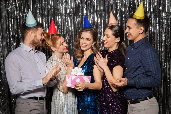 Amigos felizes em chapéus de festa com presente de aniversário — Fotografia de Stock