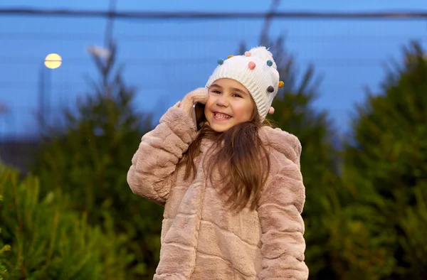 Girl calling on smartphone over christmas trees — Stock Photo, Image