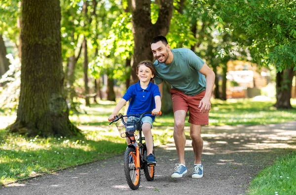 Padre enseñando a su hijo a montar en bicicleta en el parque — Foto de Stock