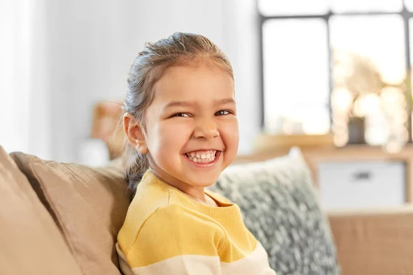 Счастливая улыбающаяся маленькая девочка, сидящая дома на диване — стоковое фото